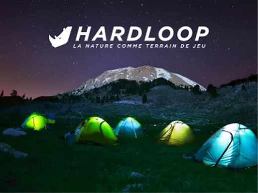 Des tentes éclairées au bivouac devant un sommet enneigé, la nuit, avec le logo Hardloop