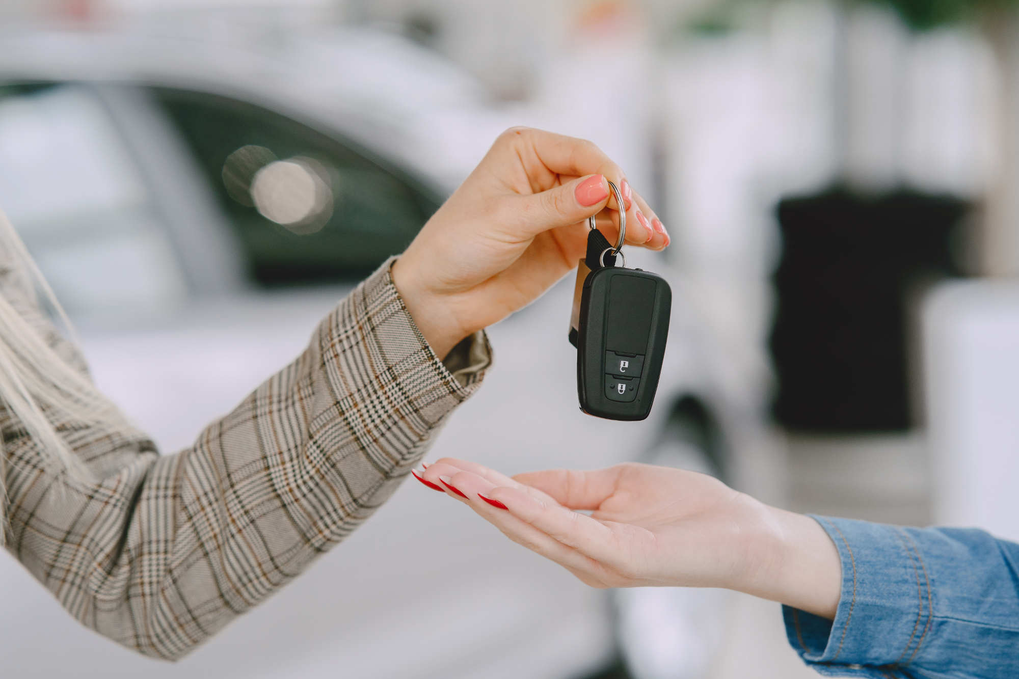 Une main tend les clés d'une voiture à une autre, devant un véhicule en concession