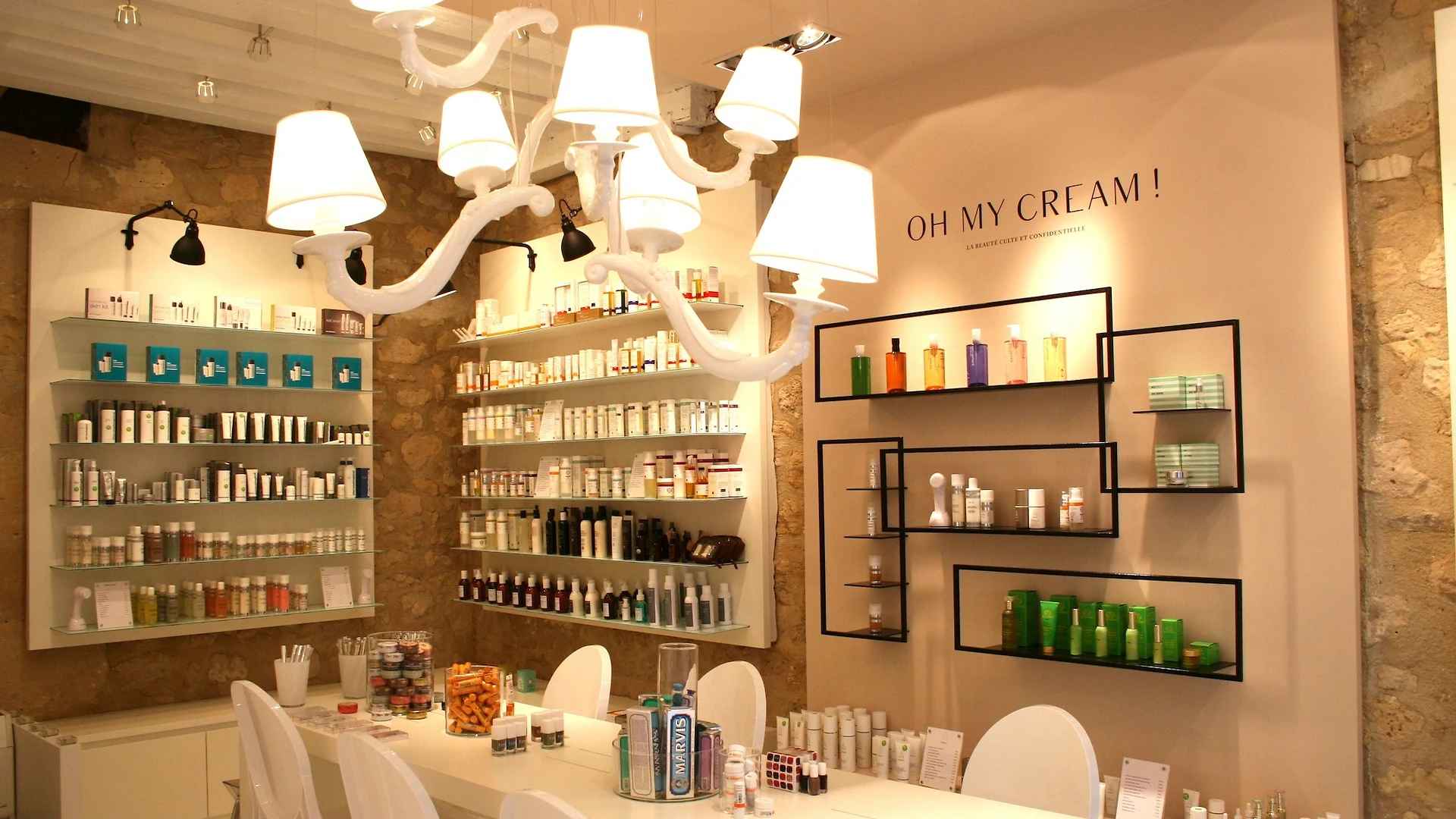 L'intérieur d'une boutique Oh My Cream : des étagères de soins sur un mur de pierre, sous un lustre blanc, et l'enseigne peinte au mur