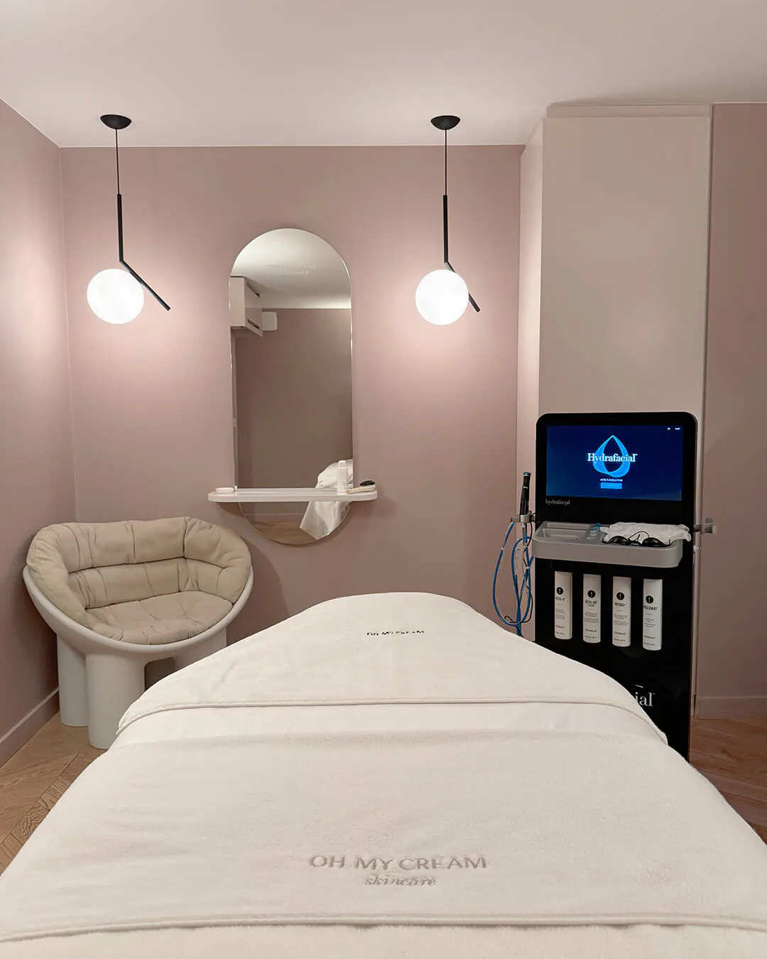 Une cabine de soin Oh My Cream : table de massage, miroir arqué et appareil de soin du visage, dans une pièce rose poudré